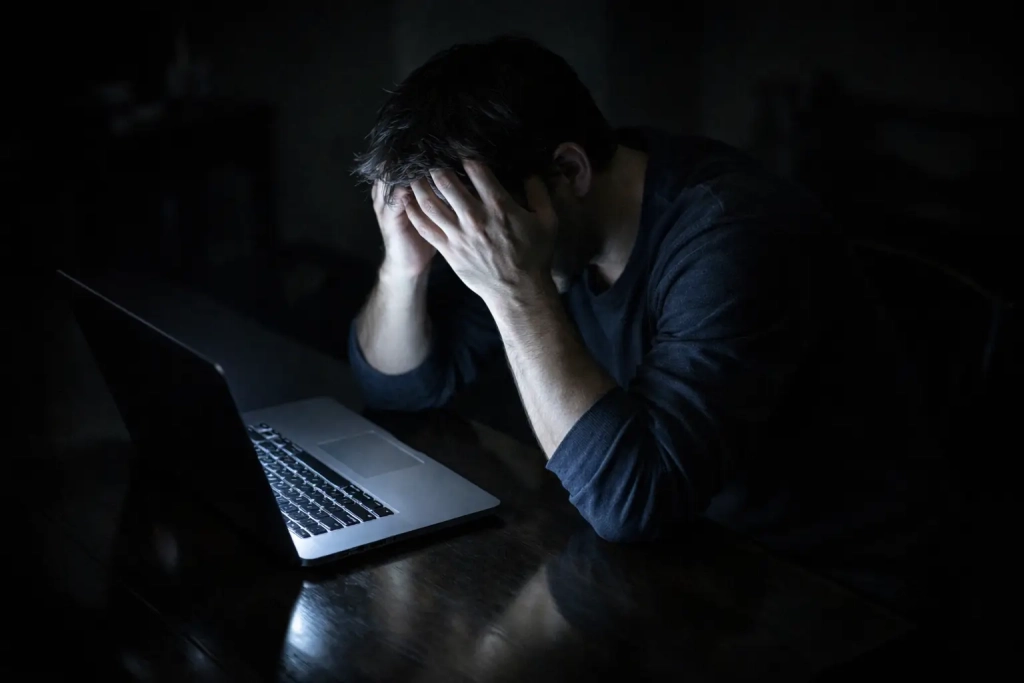 Persoon zit gefrustreerd achter laptop met hoofd in handen